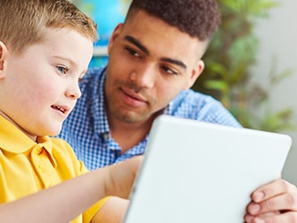 A man assists a boy with a tablet in a Medbridge session.