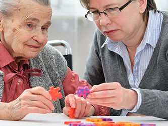 An elderly woman and a younger woman are assembling a colorful puzzle at a table.