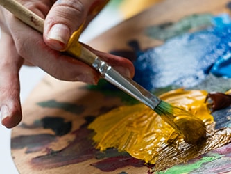 Hand blending yellow paint on a wooden palette with a paintbrush.