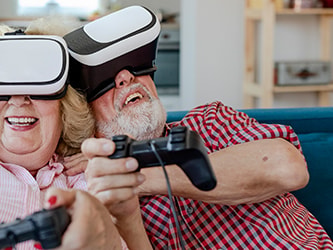 Elderly couple using VR headsets and controllers, smiling on a couch.