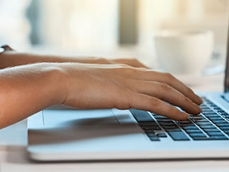 Typing on a laptop with a Medbridge coffee cup in the background.