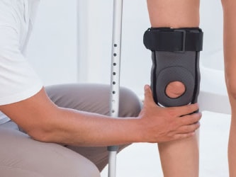 In a bright room, one person helps another with a knee brace as they stand with crutches, showcasing the medbridge product.
