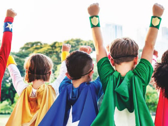 Five kids in superhero costumes, with raised fists, stand outdoors before a city skyline.