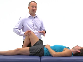 A person in a blue tank top receives a knee examination on a treatment table from someone in a white shirt.
