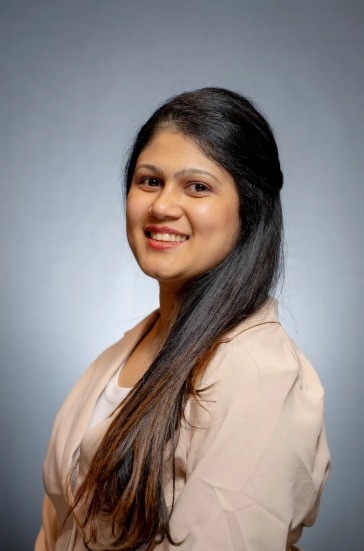 A woman with long dark hair in a light blazer smiles at the camera against a gray background, representing medbridge professionalism.