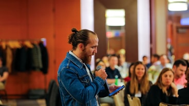 A man in a denim jacket speaks into a microphone at a medbridge conference.