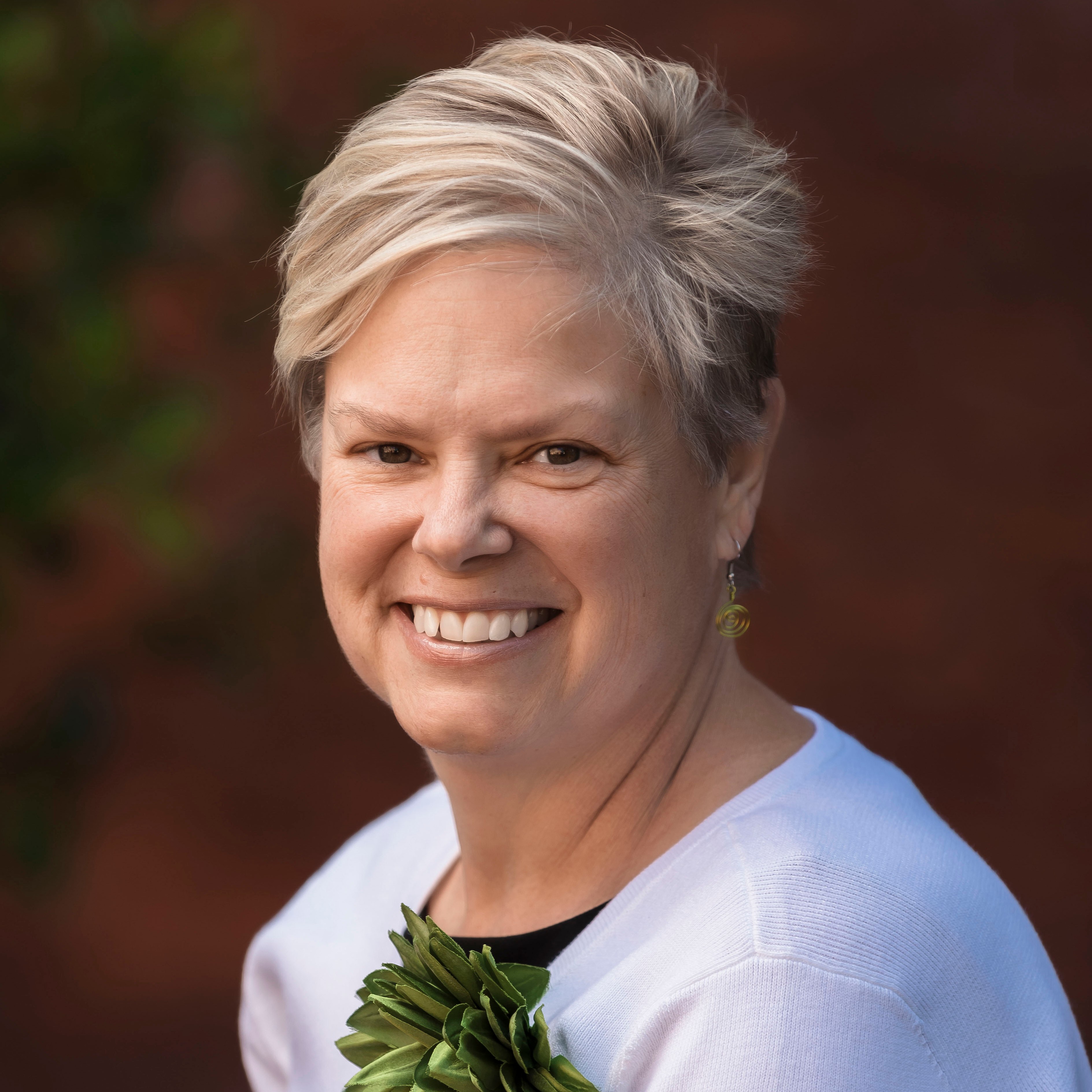 A person with short blonde hair and green earrings smiles near a plant, possibly discussing Medbridge's role in digital healthcare education.