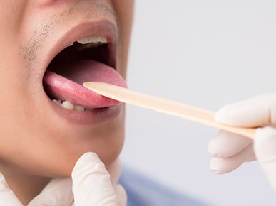 A gloved hand uses a tongue depressor to examine a person's throat during a medical exam.