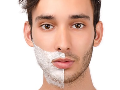 A man with shaving cream on half of his face, highlighting shaved vs. unshaved skin.