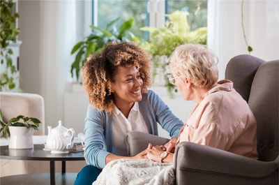 A young woman discusses healthcare training with an elderly woman in a plant-filled room, as a tea set sits nearby, reflecting their engaging conversation about digital healthcare and medbridge.