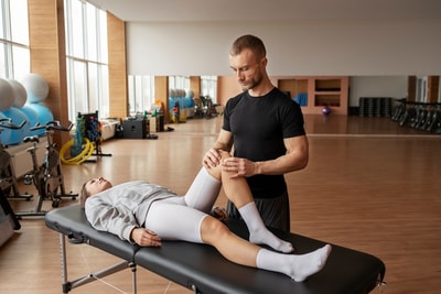 A physical therapist assesses a patient's knee amidst gym equipment and mirrors, exemplifying medbridge's hybrid care approach.