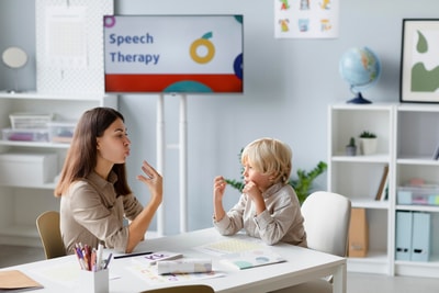 A woman and child engage in a digital Medbridge speech therapy session at a table.