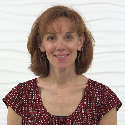 A woman with shoulder-length brown hair smiles confidently, suggesting her expertise in Medbridge's patient care software.