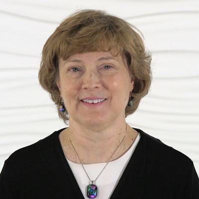A confident woman with short brown hair smiles against a white background, symbolizing the progressive spirit of hybrid care innovations in digital healthcare like medbridge.