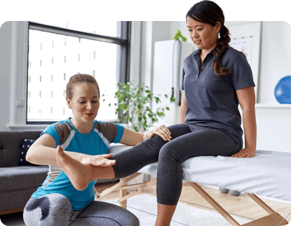 A therapist in blue evaluates a patient's leg on a therapy table, using medbridge software.