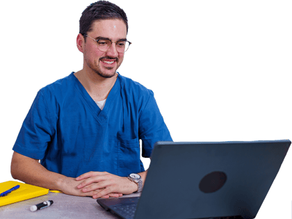 A person in blue scrubs smiles while studying digital healthcare on a laptop with medbridge, against a backdrop of pink flowers.