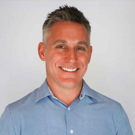 Smiling man with short gray hair in a light blue shirt stands in front of white background, representing medbridge healthcare education.