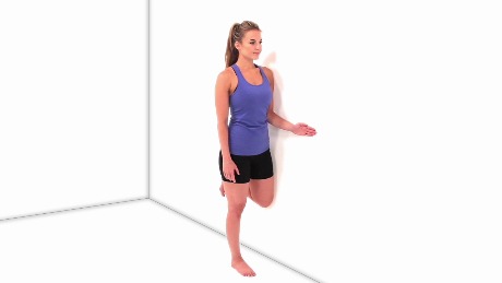 In a medbridge training, a person stands on one leg in a corner to demonstrate patient care techniques.