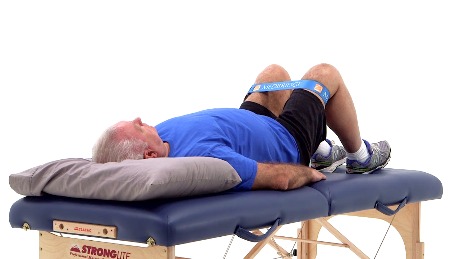 An elderly man on a therapy table uses a blue resistance band, representing hybrid care with medbridge's innovative patient software.