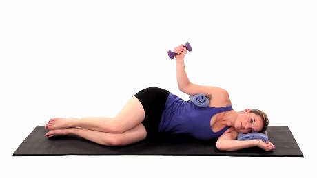 A woman on a yoga mat lifts a purple dumbbell, integrating medbridge principles into her workout.
