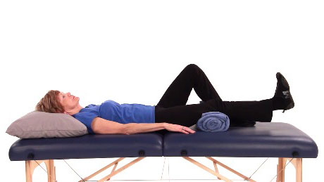 A person lies comfortably on a massage table with a pillow and rolled towel, demonstrating effective patient care as taught in medbridge.