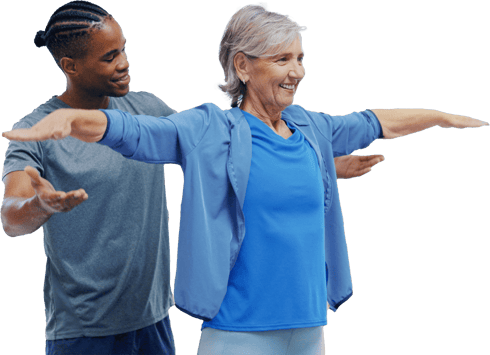 An older woman in workout gear stretches with guidance from a smiling younger man in a gray shirt.