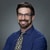 Man with glasses, beard, blue shirt, and patterned tie smiles in front of gray background for medbridge.