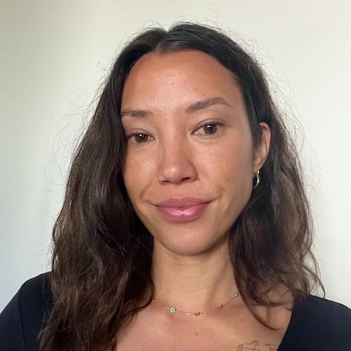 A woman with long wavy brown hair in a black top and necklace poses against a white background, representing medbridge.