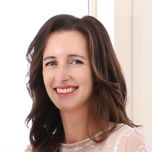 A woman with long brown hair in a white blouse smiles at the camera for medbridge.