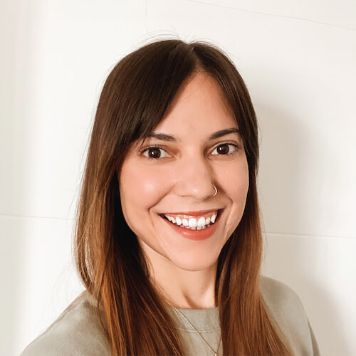 Woman with long brown hair and a nose ring, in a beige top, smiling against a plain background for medbridge.