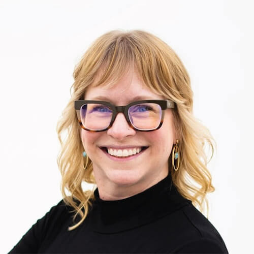 Blond person with glasses and a black turtleneck smiles against a white background, representing medbridge.