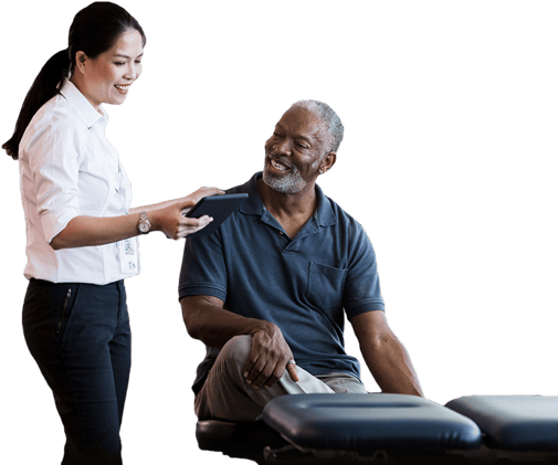 A woman shows a tablet with medbridge tools to a smiling man beside an exam table.