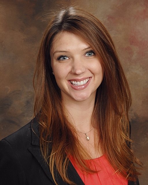 A woman with long brown hair smiles warmly, wearing a black blazer over a red top, representing healthcare education on a medbridge backdrop.