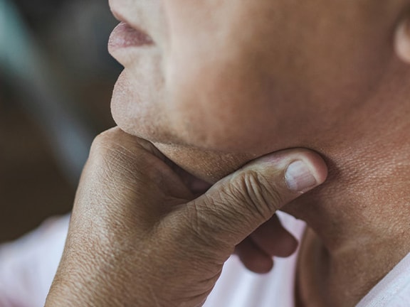 A person in a light shirt touches their throat, looking pensive or worried.