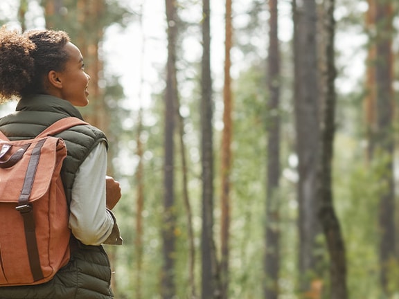 Individual with a backpack in a forest looking sideways at tall trees.