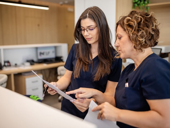 Two women in navy scrubs discuss documents at a modern desk, collaborating on medbridge digital healthcare solutions.