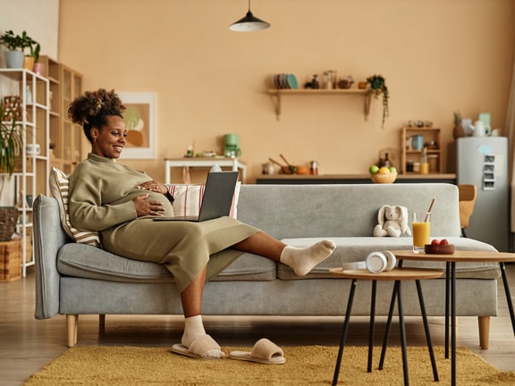 Pregnant woman using a laptop in her living room to explore medbridge digital healthcare resources.