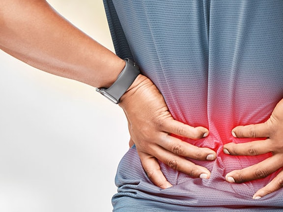 A person clutching their lower back in pain is wearing a grey shirt and watch, with a red glow highlighting discomfort.