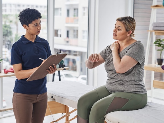 Occupational therapist taking notes while listening to a patient describe shoulder pain during a healthcare coaching session.