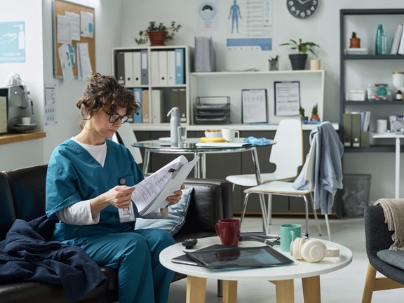 Healthcare professional in scrubs reviewing patient records in a breakroom, related to habilitative vs. rehabilitative billing.