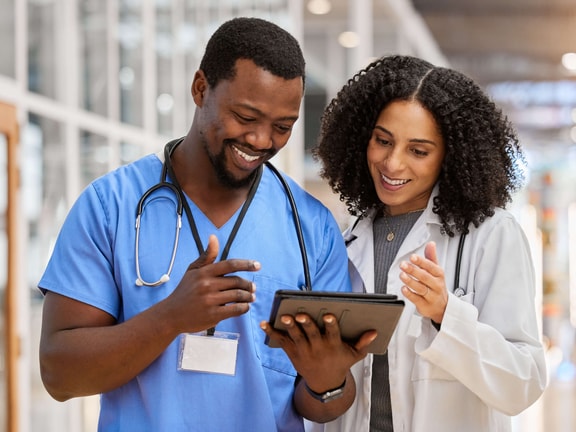Two healthcare professionals reviewing a digital tablet in a hospital setting, discussing Bundled Payments for Care Improvement (BPCI).