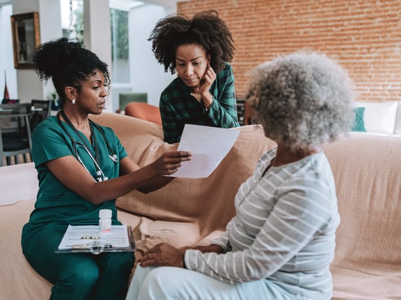 Nurse discussing care plan with an older adult and family member at home, highlighting caregiver burden in rehabilitation settings.