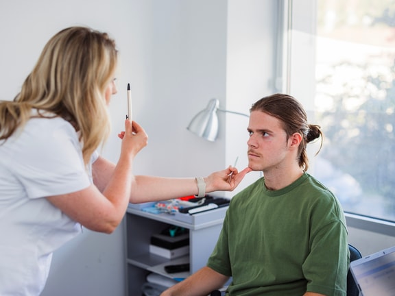 Clinician performing an oculomotor test to assess central vs. peripheral vestibular dysfunction in a seated patient.