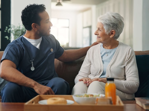 A healthcare worker talks with an older woman at home near a breakfast tray, discussing medbridge digital care.