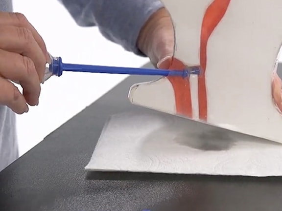 A person uses a blue applicator to fix a broken white object with red accents on a black surface.
