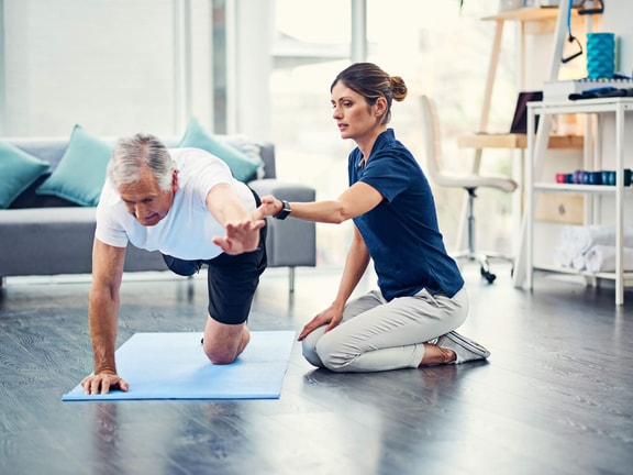 A physical therapist guides an older man through a bird-dog exercise for Medbridge training.