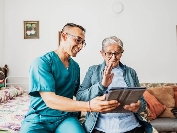Clinician reviewing an augmentative and alternative communication tablet device with an older adult patient at home