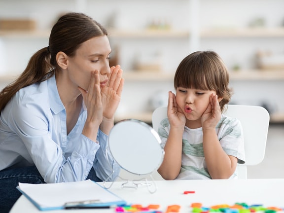Speech therapist demonstrating dynamic temporal and tactile cueing (DTTC) techniques with child during speech therapy session.