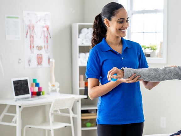 A Medbridge professional helps an older woman with arm exercises in a medical room.