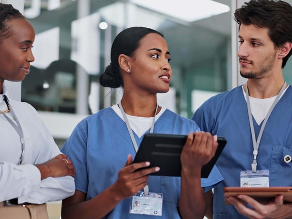 Healthcare professionals in scrubs reviewing patient information on tablets during a care team discussion, illustrating EMR vs. EHR.